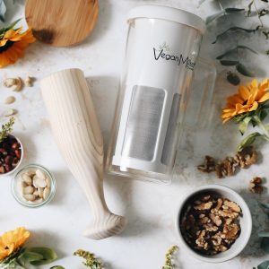 Vegan Milker con mortero de madera y cuencos con distintos frutos secos sobre una superficie blanca con pipas de girasol.