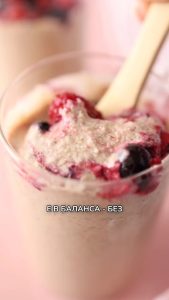 Vaso transparente con porridge de avena preparado con Vegan Milker, con frutas variadas y cuchara beige; texto en cirílico.