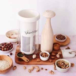 Vegan Milker con mazo de madera, frutos secos, semillas y granos en cuencos sobre tabla de madera.