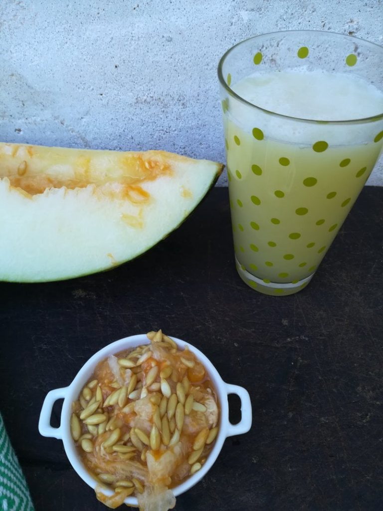 vaso con zumo de melón junto a semillas de melón y trozo de melón